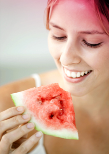 Imagem de uma jovem a comer uma fatia de melancia. A imagem ilustra uma das sugestões para aliviar as dores menstruais: comer fruta ou vegetais com elevado teor de água.