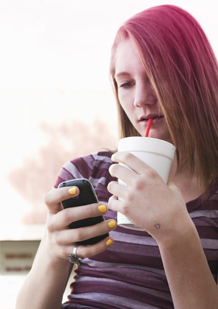 Imagem de uma rapariga a beber um refrigerante e a usar o telemóvel.